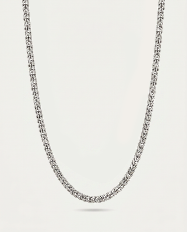 A silver-toned metallic chain necklace with a textured, woven link design, shown draped against a light off-white background.