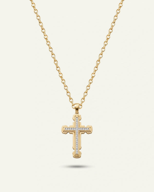 A gold cross pendant necklace with small clear stones set along the arms, hanging from a delicate gold chain against a light cream background.