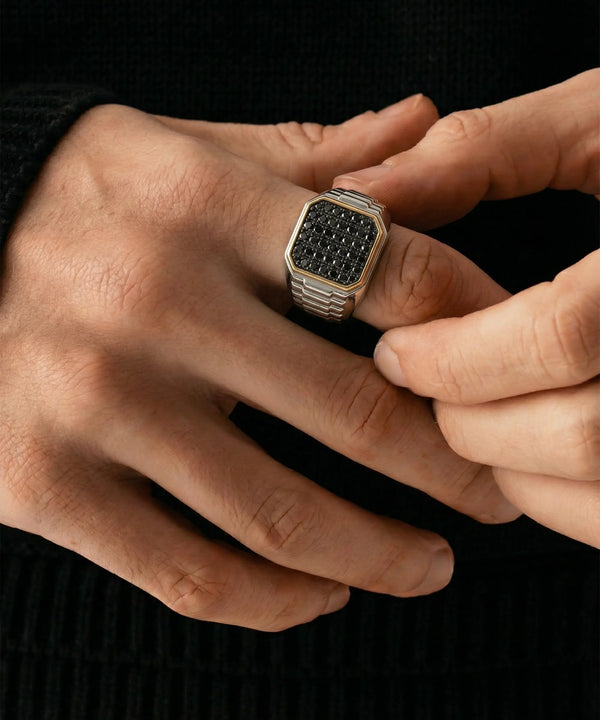 Close-up of a hand wearing a black and gold ring against a dark background