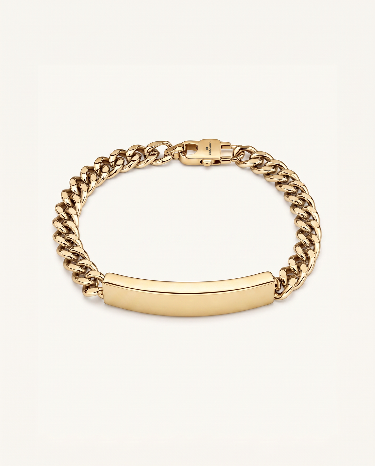 A gold-toned metal chain bracelet with a smooth, curved ID nameplate in the center, shown on a light cream background.