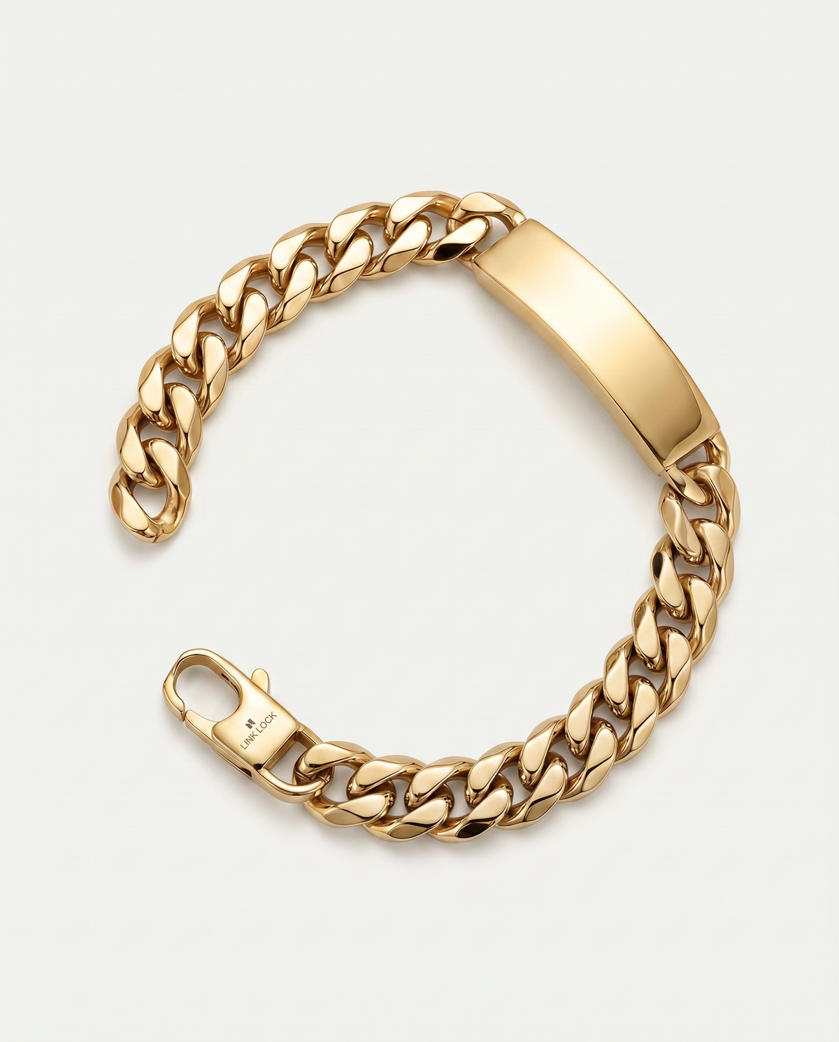 A gold-tone Cuban link chain bracelet with a polished rectangular ID plate and spring-ring clasp, shown on a light gray background.