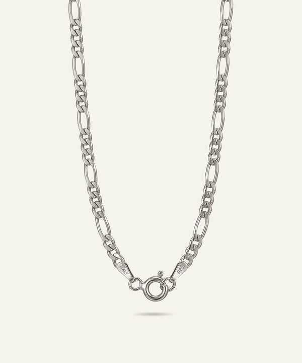 A silver Figaro chain necklace with a lobster clasp, shown against a light cream background.