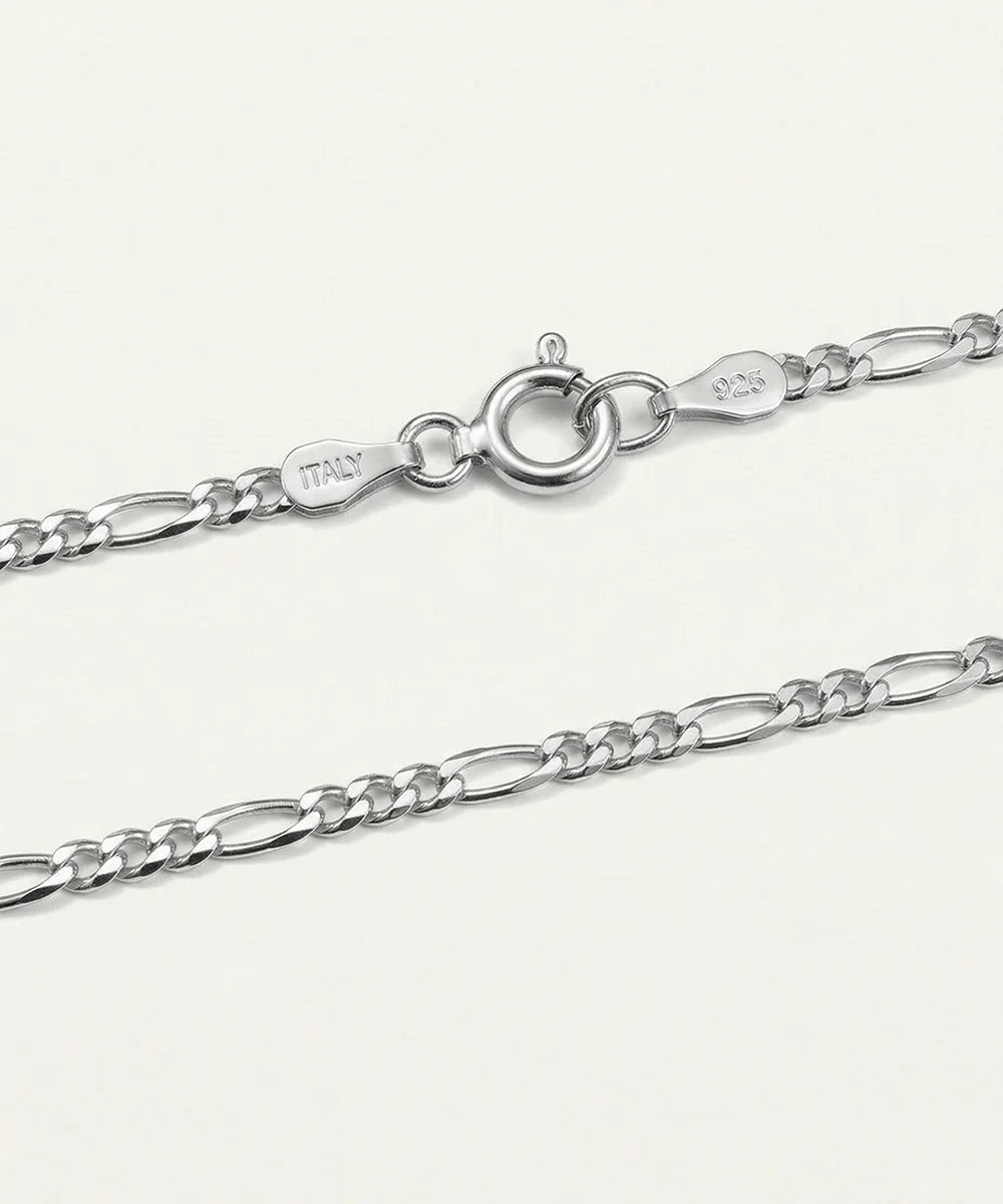 Close-up of a silver Figaro chain necklace showing the lobster clasp, a polished tag engraved with 'ITALY', and '925' sterling silver markings on a light off-white background.