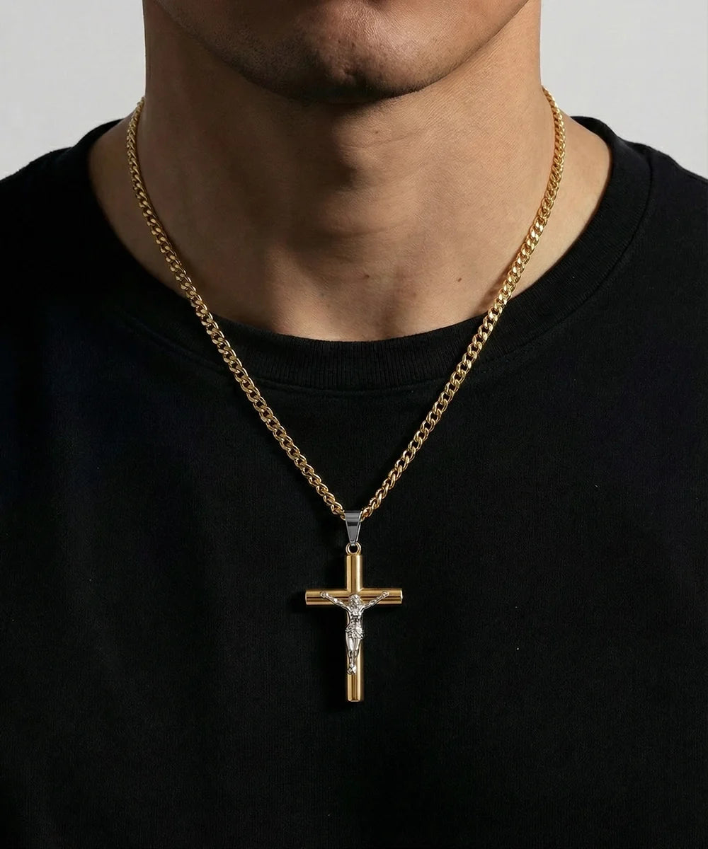 A gold crucifix pendant necklace worn by a person in a black t-shirt. The pendant features a gold cross with a silver-toned Jesus figure and a small clear gemstone at the top.