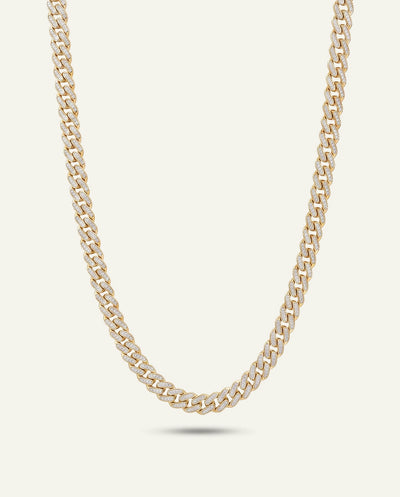 A gold-toned Cuban link chain necklace displayed in a curved U-shape against a light cream background.