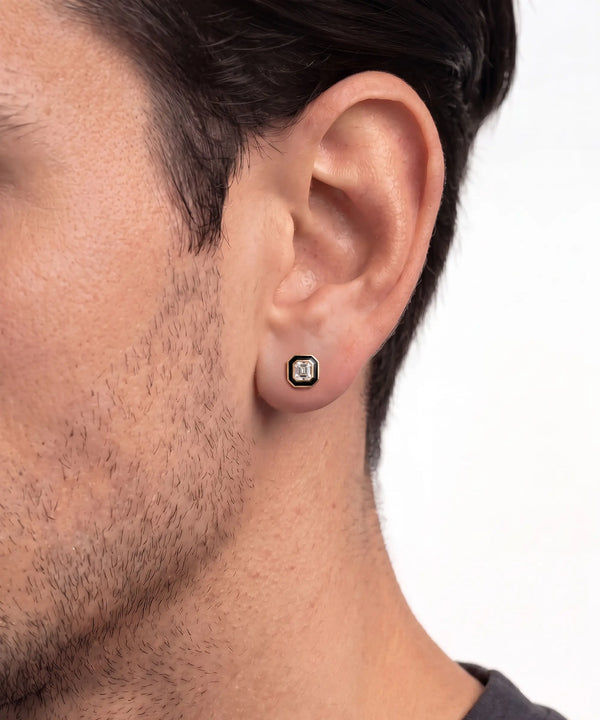 Close-up lifestyle shot of a man wearing a square gold stud earring featuring a dark central stone set in a black halo border.
