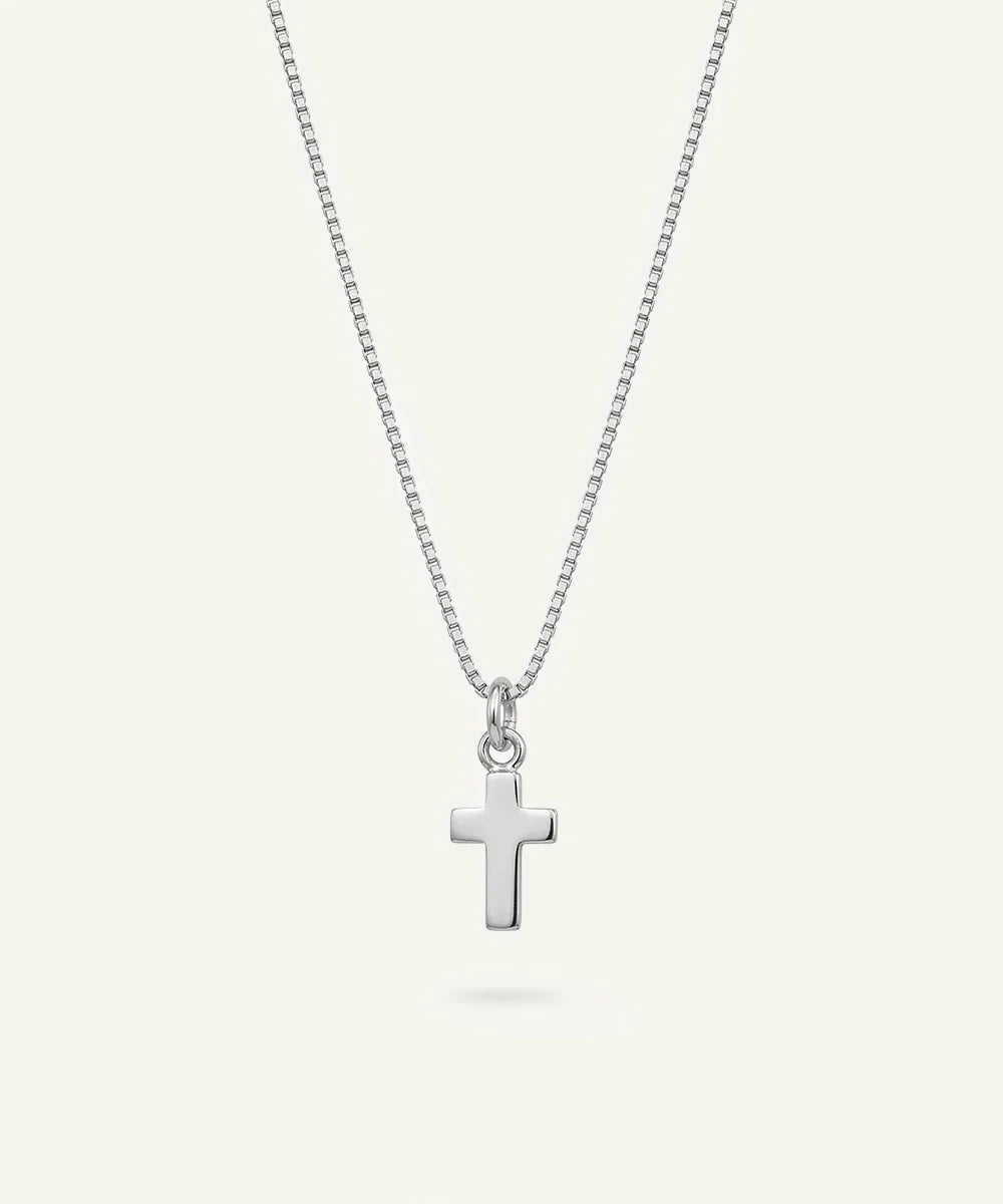 A silver cross pendant necklace on a delicate silver box chain, displayed against a solid off-white background.