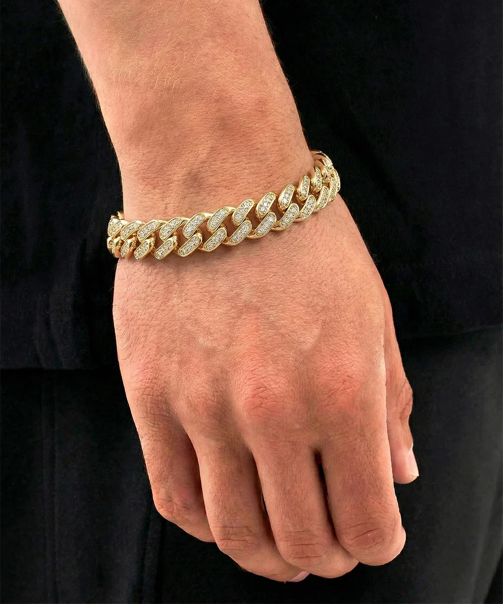Close-up lifestyle shot of a man's hand and wrist wearing a gold-toned pavé diamond-encrusted Miami Cuban link bracelet, styled against a black shirt background.
