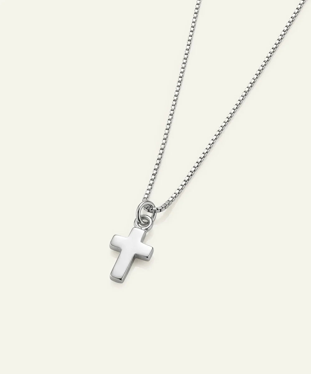A silver cross pendant necklace on a delicate silver ball chain, displayed against a solid off-white background.