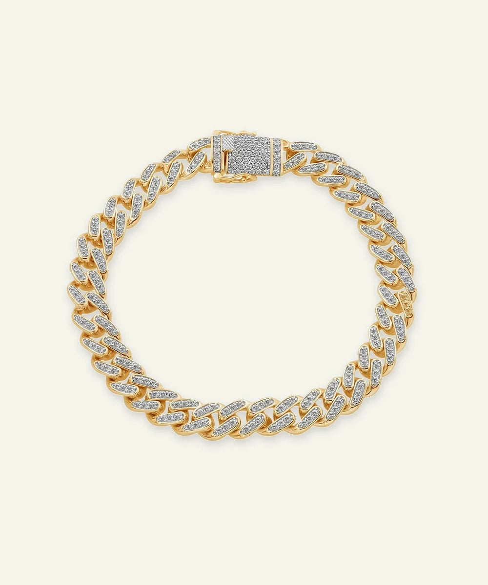 A gold-toned pavé diamond-encrusted Miami Cuban chain bracelet with a decorative clasp, displayed on a light cream background.